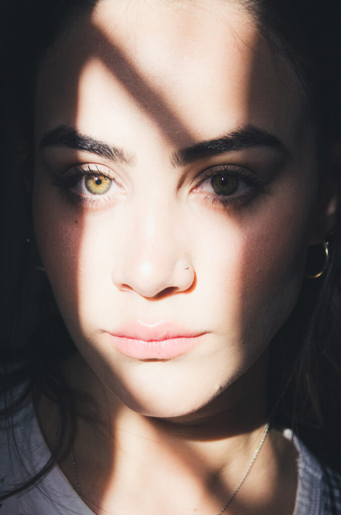 Valeria Cisneros' close-up portrait captures her intense gaze accentuated by the play of light and shadow. Her piercing green eyes detailed facial features and subtle expression convey a sense of depth and emotion.